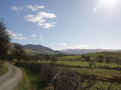 a road in a field with mountains in the background at Binsey Lodge in Wigton