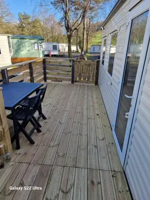 a wooden deck with a picnic table and a building at Forest Valley Holiday Home in Ballantrae