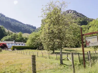 a fence with a tree in a field with a sign at Bramble Cottage in Keswick
