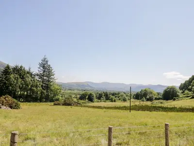 a field with a fence and mountains in the background at Bramble Cottage in Keswick