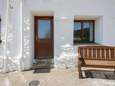 a white building with a wooden door and a bench at Bramble Cottage in Keswick