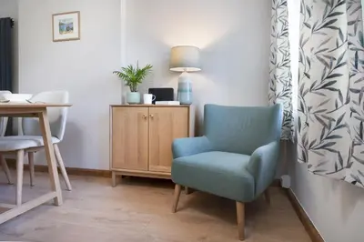 a living room with a blue chair and a table at Riverside - Quaint County Cottage overlooking the Beck in Caldbeck
