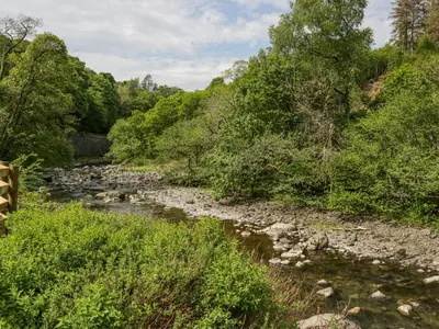 a river in the middle of a field with trees at Sail Luxury Family Pod in Keswick