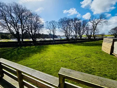 a wooden bench sitting in a field with trees at The Canny View at Three Lochs Holiday Park in Balminnoch 3 bedroom sleeps upto 8 guests in Newton Stewart
