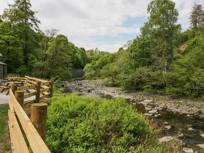 a river with a wooden fence next to a river at Woof Luxury Family Pod in Keswick
