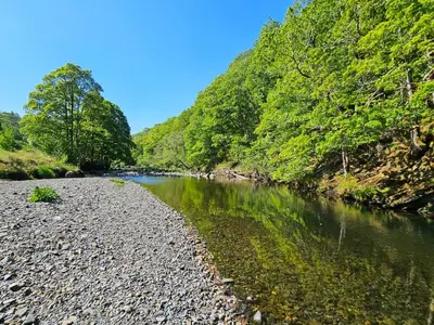 a river with rocks and trees on the side of it at Woof Luxury Family Pod in Keswick