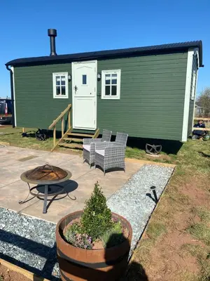 a green tiny house with a patio and a table at Sunset Snug Shepherd hut in Penrith