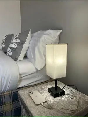 a lamp on a table in front of a bed at 5BR House w Garden Near Stadium in Moffat
