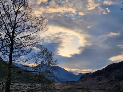 a cloudy sky with a tree and a mountain at Blea Tarn Farmhouse B&B in Ambleside