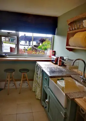 a kitchen with a sink and a counter with two stools at Cosy cottage near Thornhill in Closeburn