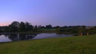 a pond in a field with a grassy field at Barmoffity Shepherds Hut in Kirkpatrick Durham