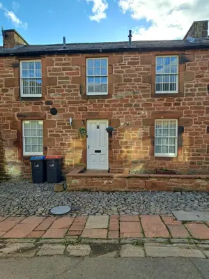 an old brick house with a white door at 2 Hares Den in Annan