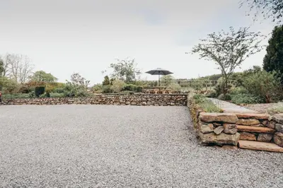 a garden with a stone wall and an umbrella at North Lakes - The Byre Holiday Cottage in Penrith