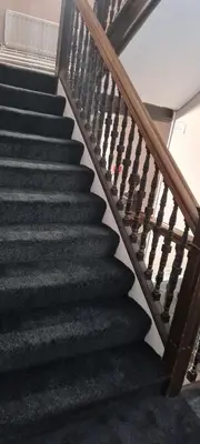 a staircase with black treads and a wooden rail at LSO Guest House in Dumfries