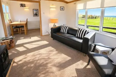 a living room with a black leather couch and a table at Stunning Sea View - Farm Stay - Kilchoman 9 in Stranraer