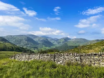 a stone wall in a field with mountains in the background at Autumn Leaves in Keswick