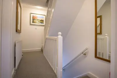 a hallway with white walls and stairs with a mirror at Moss Crag in Penrith