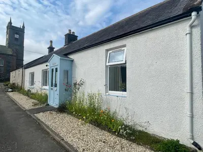 a white house with a blue door on a street at Glencairn Cottage in Moffat