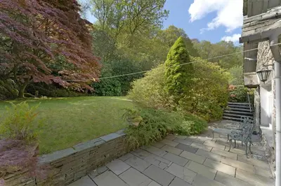 a garden with a bench and a lawn with trees at Poet's View Cottage in Grasmere