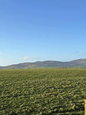 a large field of grass with mountains in the background at Peaceful Seaside Getaway in Mainsriddle