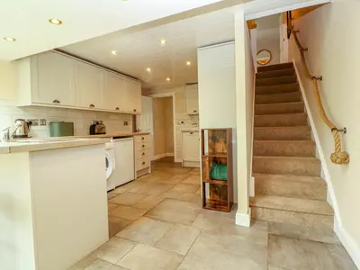 a kitchen with a staircase and a kitchen with white cabinets at Kirkland Howe Cottage in Frizington