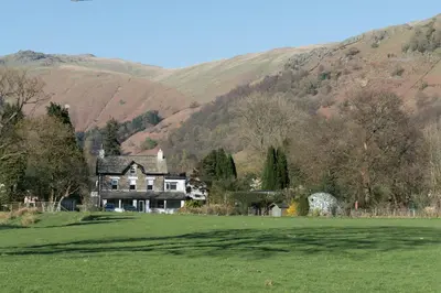 a house in a field with mountains in the background at Lake View Country House and Self-catering Apartments in Grasmere