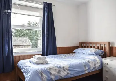 a bedroom with a bed with blue curtains and a window at Crag Barn Cottage Lake District by PolkaStays in Penrith