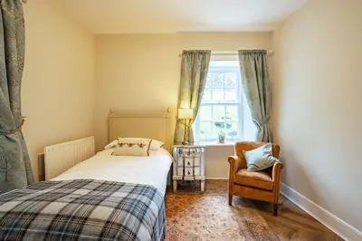 a bedroom with a bed and a chair and a window at Penninghame Estate- Gardeners Cottage in Challoch