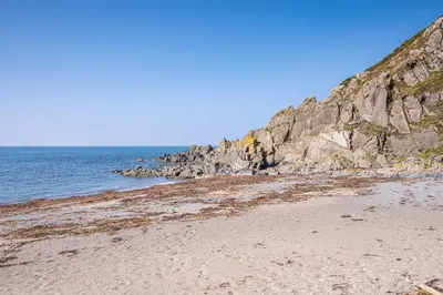a sandy beach next to the ocean with a rocky cliff at Knockinaam Lodge in Portpatrick
