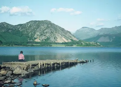 a man sitting on a dock near a lake at Sycamore Cottage, Western Lakes Bolthole With Views Across the Fells in Arlecdon