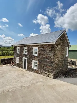 a stone house with a solar roof on a driveway at Ballavelt in Isle of Man