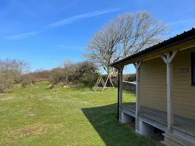 a house with a porch next to a field at Newly built luxury cabin in Moffat