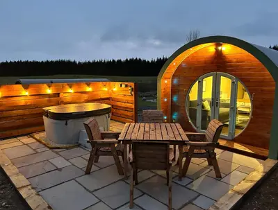 a patio with a table and chairs and a tub at Barnharrow Holiday Pods - Rose Glamping Pod with Hot Tub & Fire Pit in Balminnoch