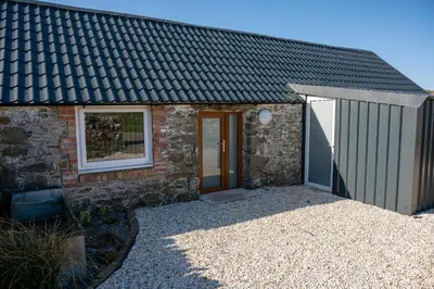 a stone house with a black roof and a door at The Larroch Byre in Monreith