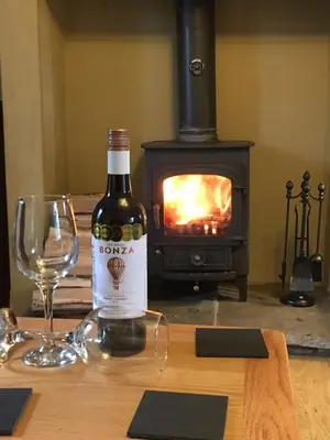 a bottle of wine and a glass on a table with a stove at Charming cosy Lakeland cottage near Ullswater in Dacre