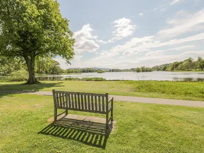 a park bench sitting in the grass near a lake at King's Apartment in Castle Douglas