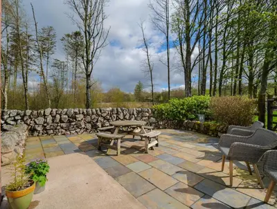 a patio with a table and chairs and a stone wall at Hill View at Kenmuir in Dalbeattie