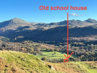 an old school house on a hill with mountains in the background at The Old School House - Eskdale in Holmrook