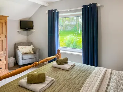 a bedroom with a bed with a window and a chair at Gillhead Farm Cottage in Troutbeck