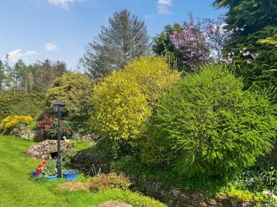 a garden with flowering bushes and a lamp post at Gillhead Farm Cottage in Troutbeck