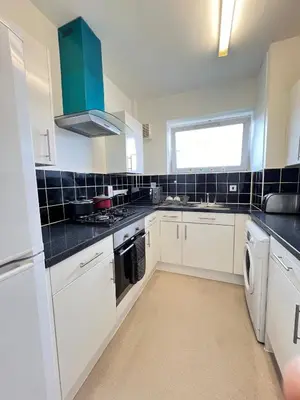 a kitchen with white cabinets and a blue tiled wall at Flat in London Bridge in Moffat
