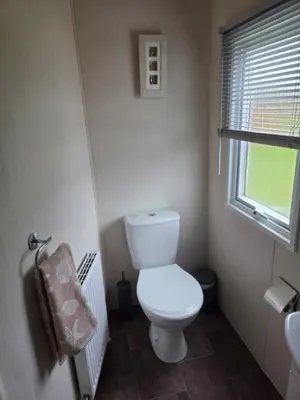 a bathroom with a toilet and a window and a sink at Lovely Caravan number 96 at Three Lochs Holiday Park in Kirkcowan