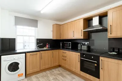 a kitchen with wooden cabinets and a washer and dryer at Lovely 2 Bed Harbourside Apartment with Sea Views in Whitehaven