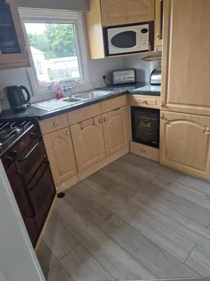 a kitchen with wooden cabinets and a sink and a microwave at Shep2 Caravans in Ballantrae