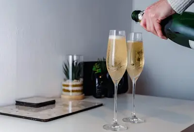 a person pouring champagne into two champagne glasses on a counter at Bega House Apartment in Whitehaven