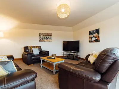 a living room with leather furniture and a flat screen tv at Middle Byre in Girthon