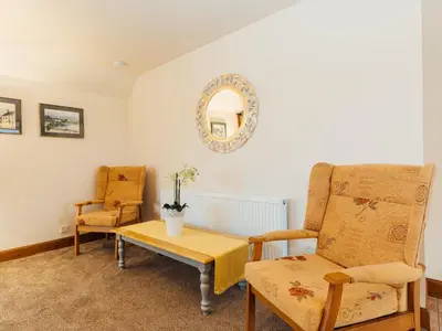 a living room with a chair and a table and a mirror at Middle Byre in Girthon