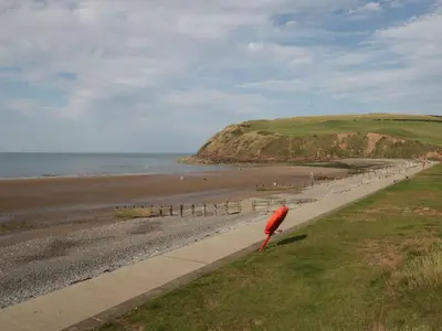 a beach with a red umbrella sitting on the grass at Lowther Suite in Whitehaven