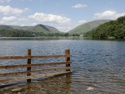a fence on the edge of a lake with mountains at Shelley in Ambleside