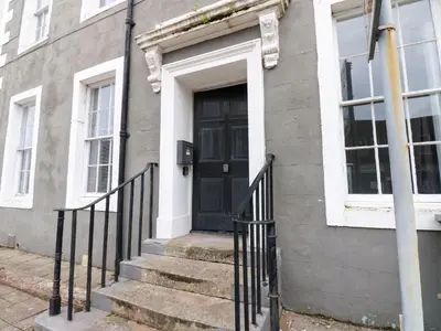 a black door on a gray house with stairs at Lowther Apartment in Whitehaven